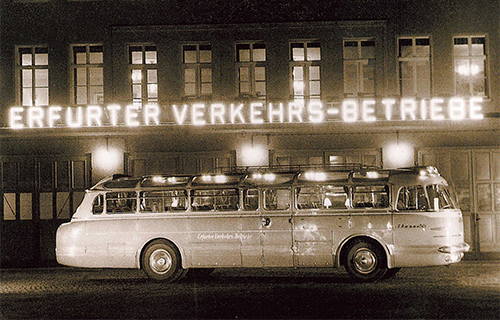 Schwarz-wei&szlig;es Bild von historischem Bus vor einer Leuchtreklame "Erfurter Verkehrs-Betriebe"