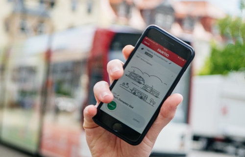 Hand mit Handy und App FAIRTIQ vor Stadtbahn