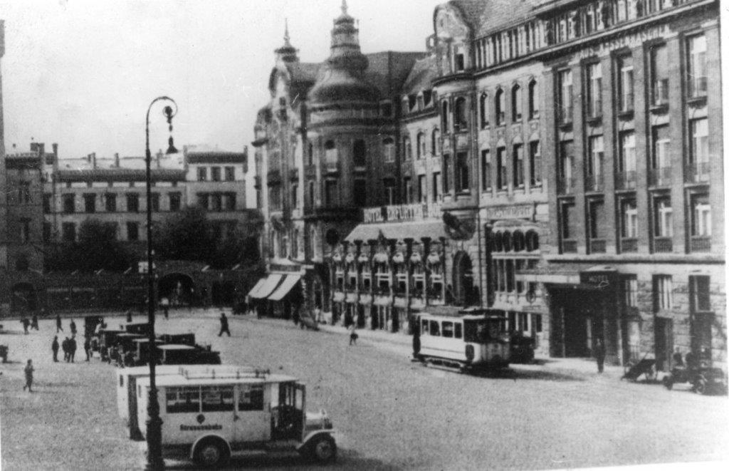 Bahnhofsvorplatz mit Triebwagen auf der braunen Linie und zwei Omnibusse.